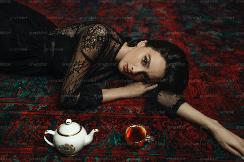 زنی که روی فرش در کنار فنجان چای و قوری دراز کشیده